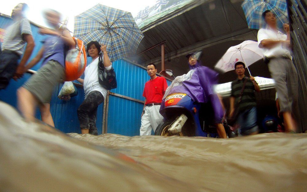 Inwoners van de Chinese stad Huhan lopen door ondergelopen straten. Foto EPA