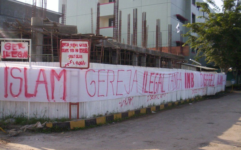 Moslimdemonstranten hingen begin dit jaar de bouwplaats van een kerk in Bekasi vol met meterslange spandoeken. „De kerk is volgens de moslimgemeenschap illegaal zonder bouwvergunning”, staat er met rode grafittiletters op de omheining. Foto J. C. Lepeltak