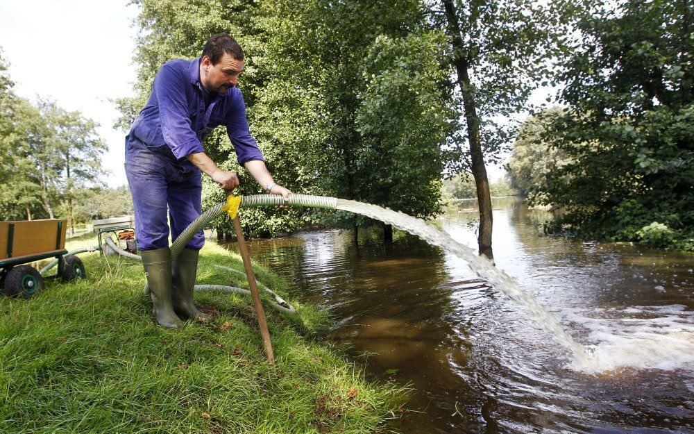 LOSSER - Frank Teunis aan de Bentheimerstraat in De Lutte probeert met een pomp het water van De Dinkel buiten de deur te houden. De rivier de Dinkel is zaterdag buiten haar oevers getreden door zware regenval. Foto ANP