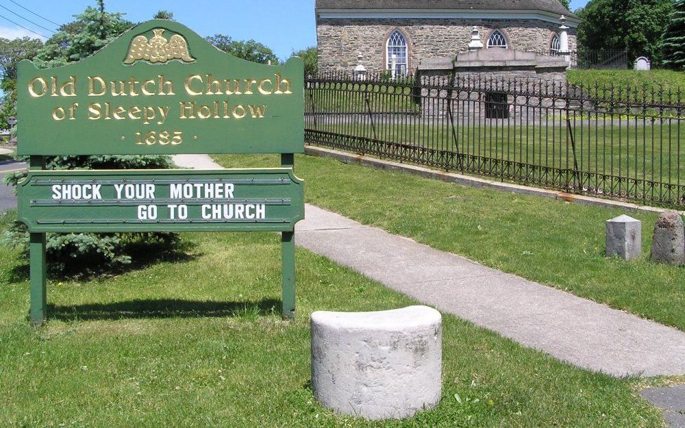 ”Choqueer je moeder, kom naar de kerk”, grapt het bord van de Old Dutch Church van Sleepy Hollow. Het Amerikaanse kerkje heeft wortels in de 17e-eeuwse kolonie Nieuw-Nederland. Foto Wikipedia