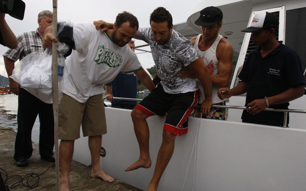 De Australische surfer Robert Marino wordt aan land geholpen in West Padang. De Australier overleefde samen met negen andere surfers de tsunami. Foto EPA