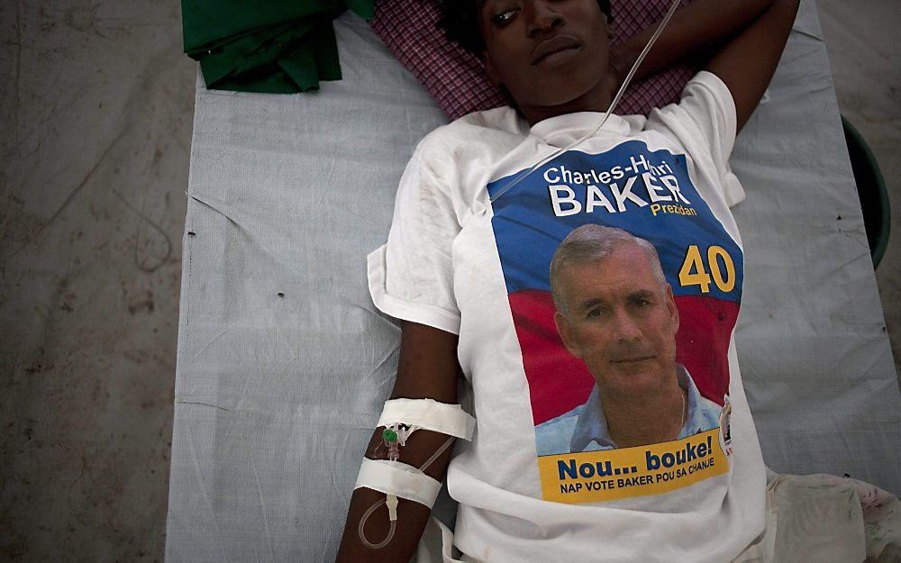 Een Haïtiaanse cholerapatiënte wacht op medische behandeling voor het Bicentenaireziekenhuis in Port-au-Prince. Ze draagt een campagneshirt van presidentskandidaat Henri Bakker.	Foto EPA