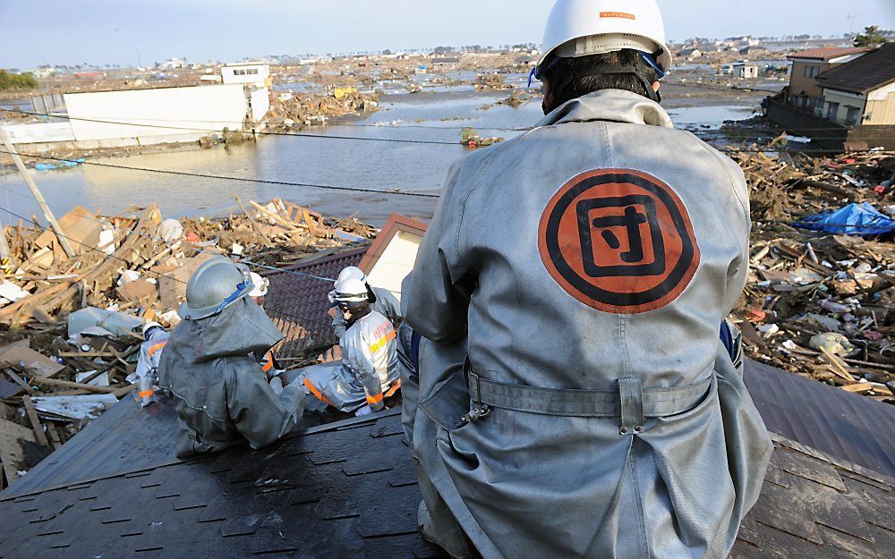 SENDAI – Brandweerlieden wachten op het dak van een huis in Sendai af of naschokken een nieuwe tsunami veroorzaken. Hulpverleners zijn op grote schaal gaan zoeken naar slachtoffers van de overstroming en mogelijk zelfs naar overlevenden. Foto Kjeld Duits