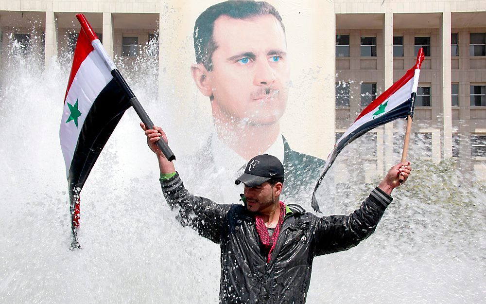 Een Syriër zwaait met vlaggen voor een portret van Assad. Foto EPA