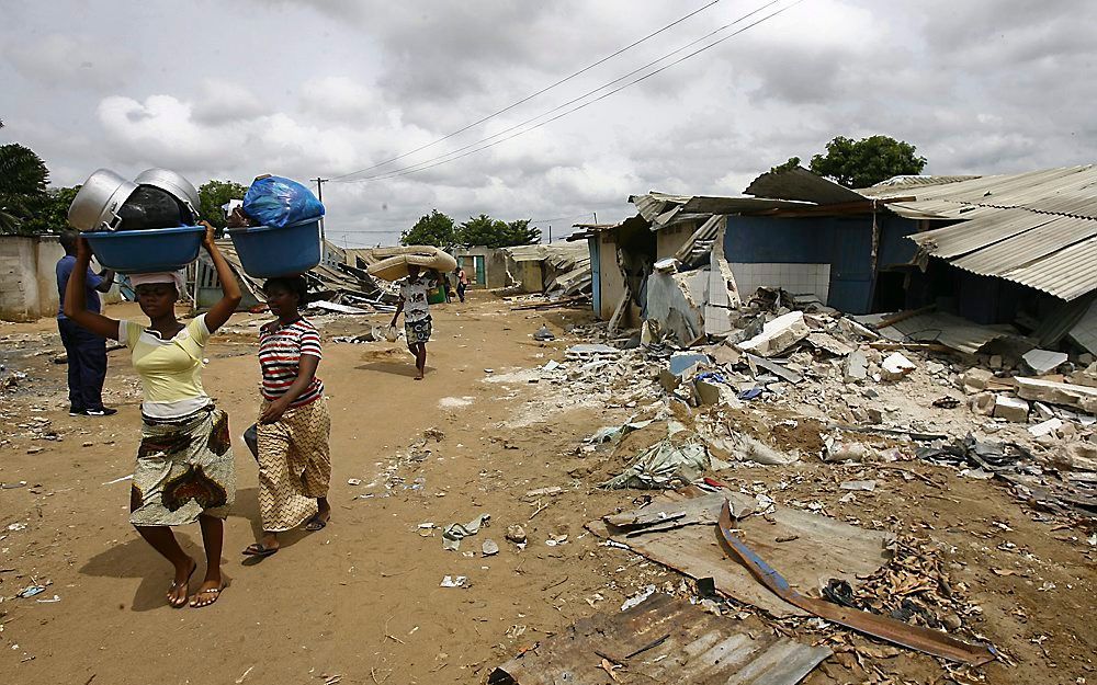 Vrouwen lopen langs verwoeste huizen nabij Abidjan, Ivoorkust. Foto EPA