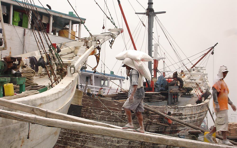 JAKARTA – Aziatische gestaltes gaan gebukt onder het gewicht van twee op elkaar gestapelde zakken meel van elk 25 kilo. Het is balanceren vanaf de kade, over smalle en doorbuigende loopplanken, op weg naar het ruim van klaarliggende, traag ogende schepen 