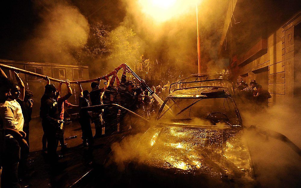 Een in brand gestoken politie-auto wordt geblust. Foto EPA