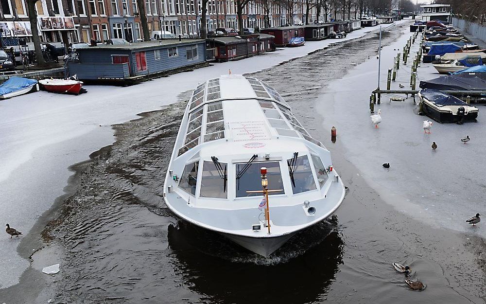 Een rondvaartboot baant zich een weg door de bevroren grachten in Amsterdam. Foto ANP