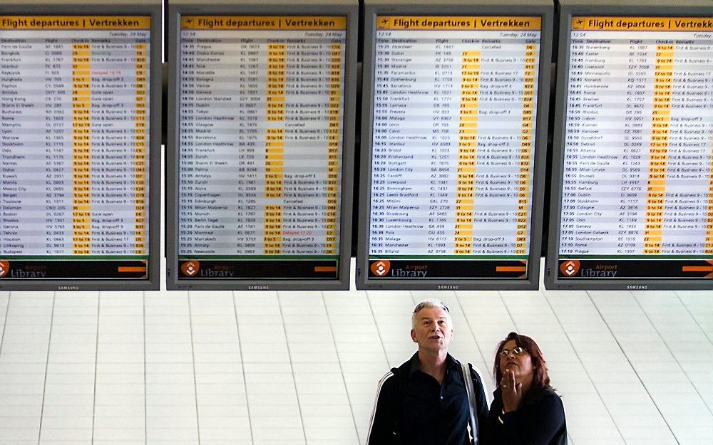 Reizigers bekijken het bord met aankomst- en vertrektijden op Schiphol.  Foto ANP