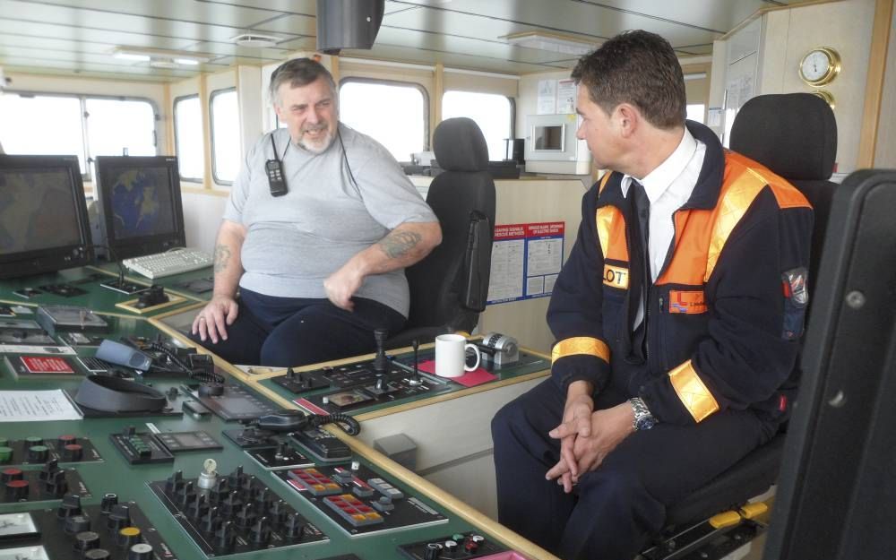 Loods Yoeri Schinkel (r.) achter het bedieningspaneel van het Ierse schip Arklow Raven, dat van de Sloehaven in Vlissingen richting open zee vaart. De kapitein (l.) ontvangt hem hartelijk. Hij is blij dat hij even de tijd heeft om wat papierwerk af te han