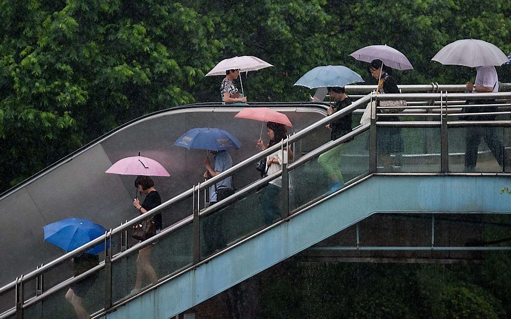 Forenzen onderweg in Shanghai, maandag. In het oosten van China is het regenseizoen begonnen. beeld AFP