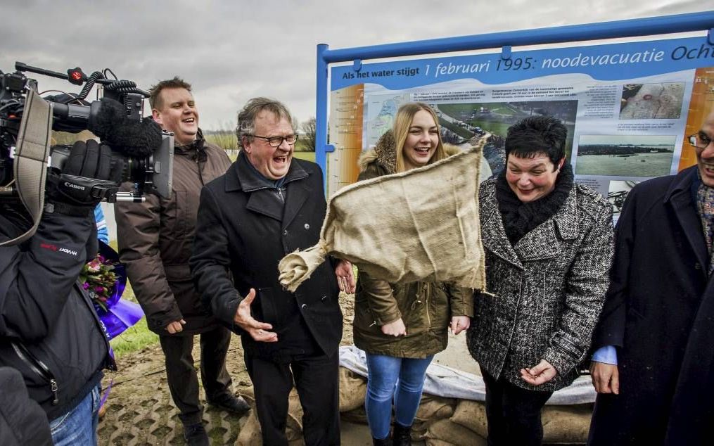 Oud-burgemeester Zomerdijk gooide zaterdag een zandzak tijdens de onthulling van een herdenkingsbord op de dijk bij Ochten. Naast hem Sanne van Lent, die tijdens de evacuatie in Winterswijk werd geboren. beeld ANP