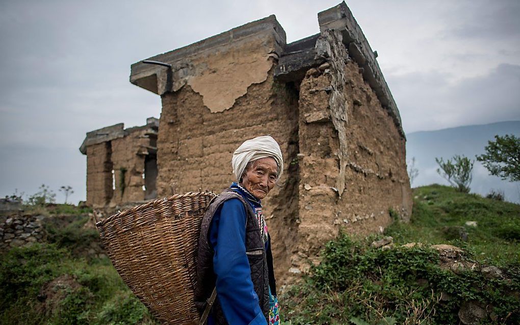 Een oudere vrouw van de Qiang-minderheid voor haar oude woning in Wenchuan, die door de aardbeving van 2008 beschadigd raakte. beeld AFP