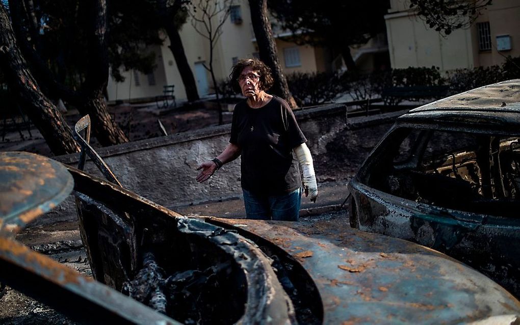 Een vrouw staat tussen uitgebrande auto's in het Griekse Mati, in de buurt van Athene. De regio werd getroffen door ernstige bosbranden. beeld AFP