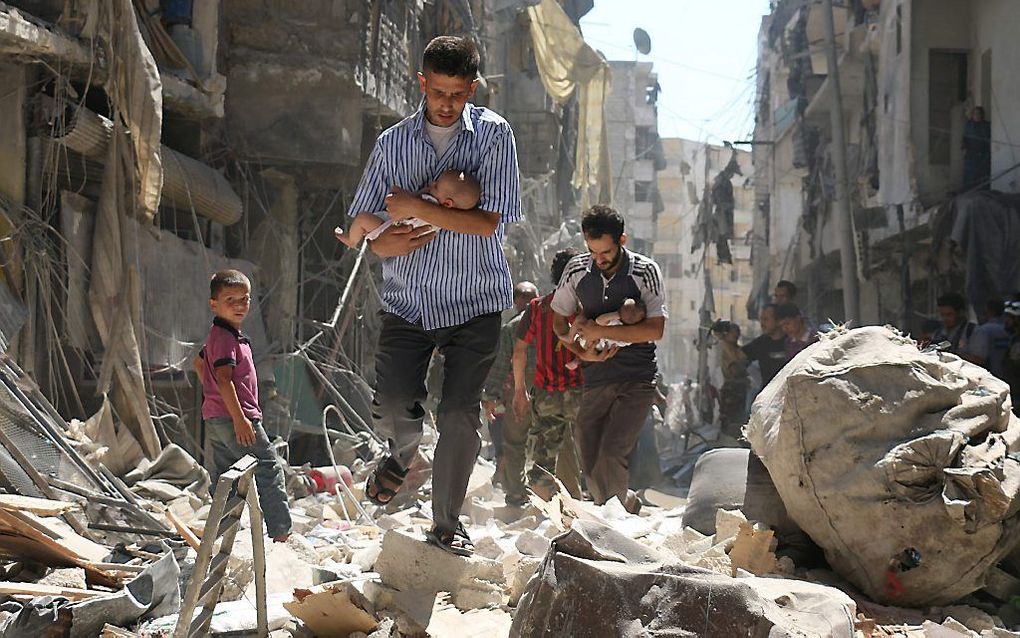 Twee Syrische mannen rennen met hun baby's door de puinhopen in de stad Aleppo. beeld AFP