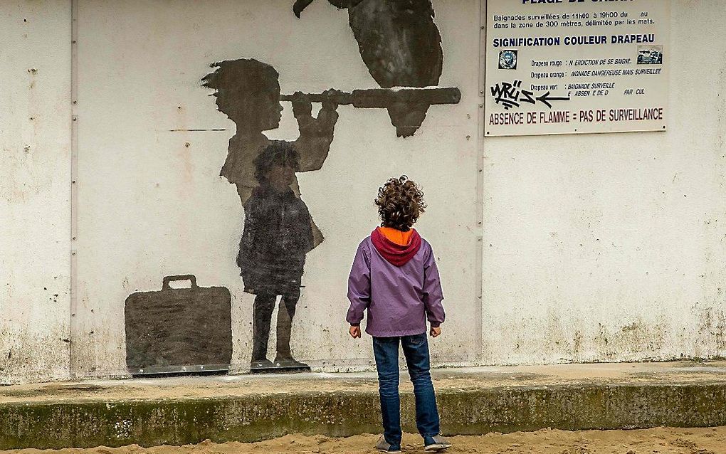 Een kind kijkt naar een werk van de Britse kunstenaar Banksy in een vluchtelingenkamp bij Calais. beeld AFP