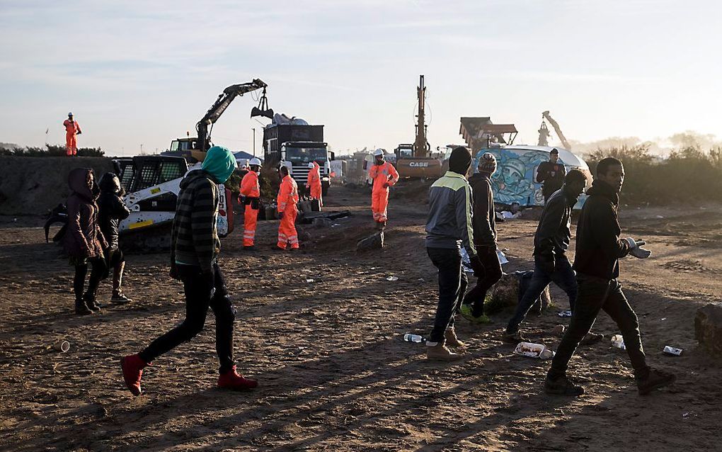 Migranten lopen voorbij terwijl werklui op de achtergrond bezig zijn met het ontmantelen van de Jungle. beeld EPA