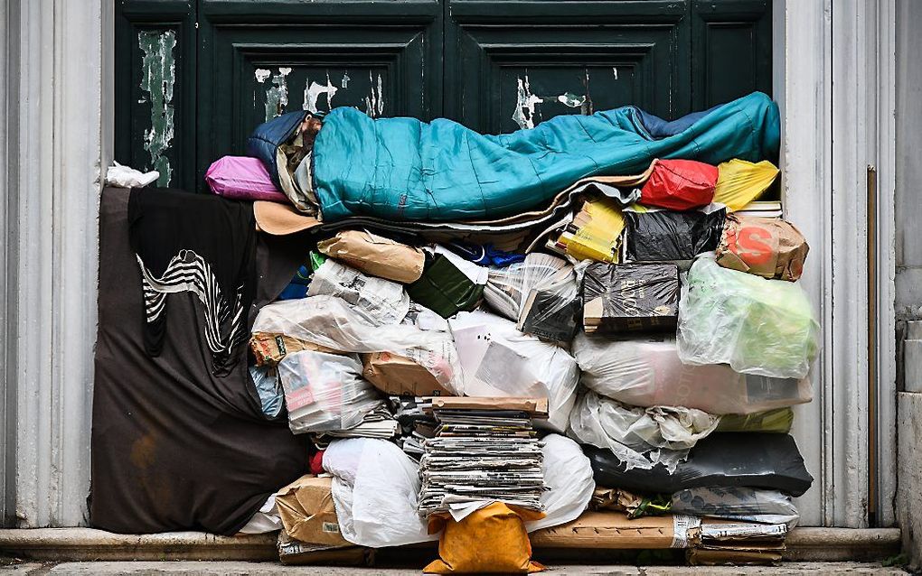 Een dakloze man slaapt op een stapel plastic zakken en kranten tegen een deur in de Italiaanse hoofdstad Rome. beeld AFP