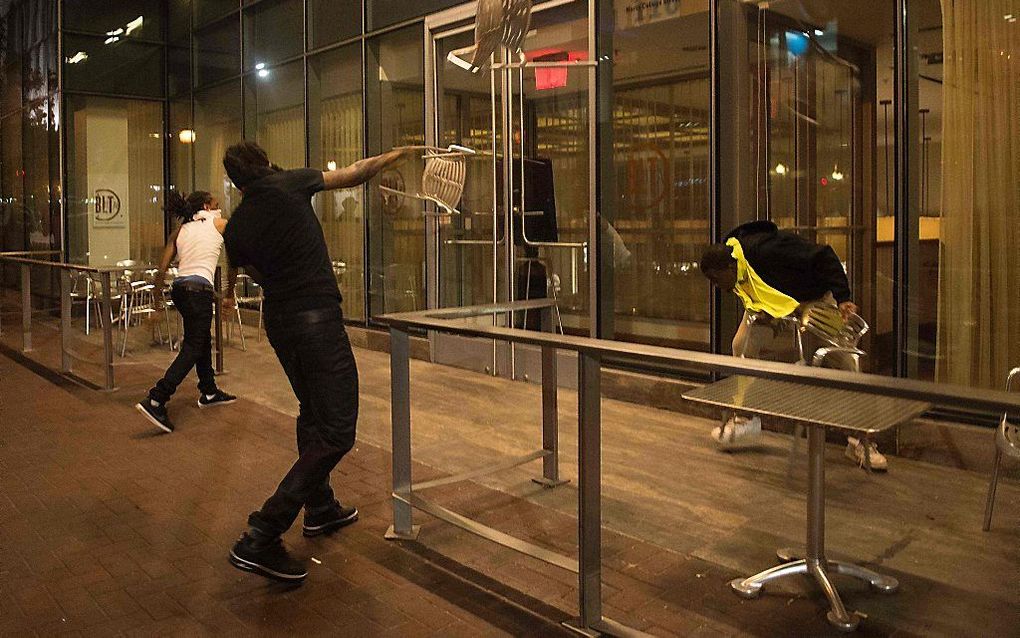 Een demonstrant gooit een stoel door de raam van een restaurant in Charlotte. beeld AFP