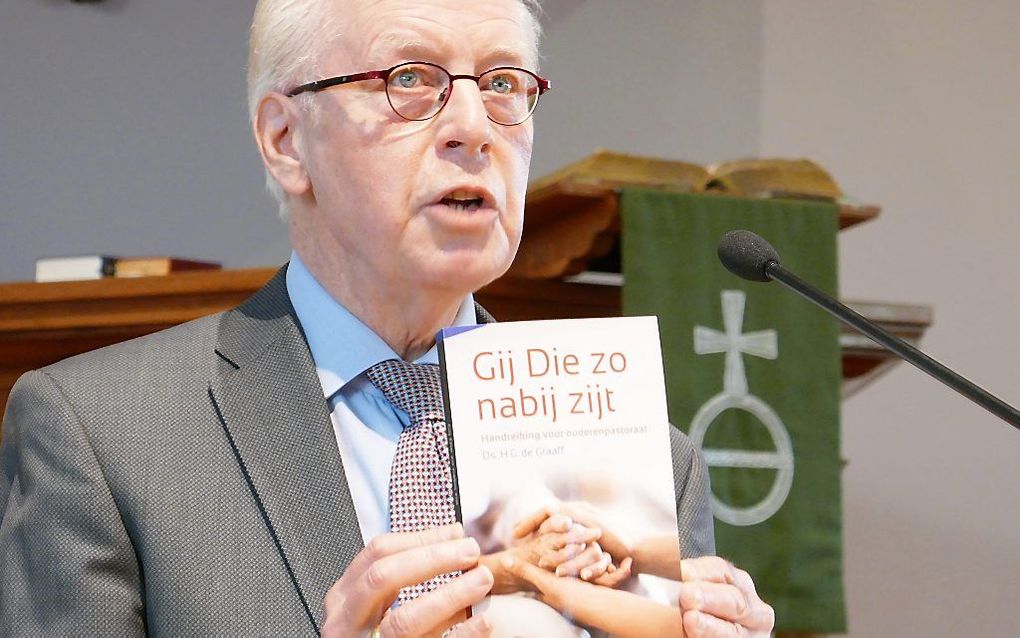 Ds. De Graaff toont in elkaar gevouwen handen op de omslag van zijn boek. beeld RD