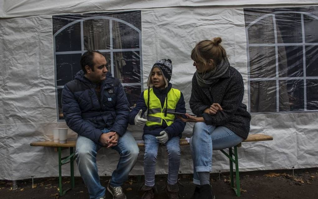 Het gesprek tussen vluchteling (l.) en vrijwilligster (r.) verloopt via een 10-jarig vluchtelingenmeisje. Ze tolkt van het Arabisch naar het Engels. Ze hoort er helemaal bij en mag daarom een hesje aan. beeld Pierre Heijboer