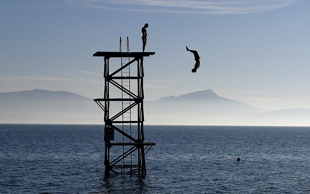 Mannen genieten van een uitzonderlijk warme herfstdag bij het meer van Geneve. beeld AFP