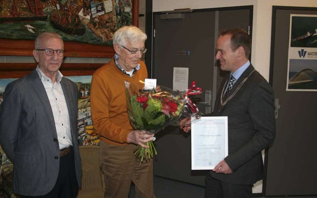 Burgemeester Van Hemmen (r.) overhandigt Gijs Lavooij (m.) een bos bloemen na het uitreiken van de bronzen legpenning van het Carnegie Heldenfonds. Lavooij redde in 1946 Kees Alblas (l.). beeld André Bijl