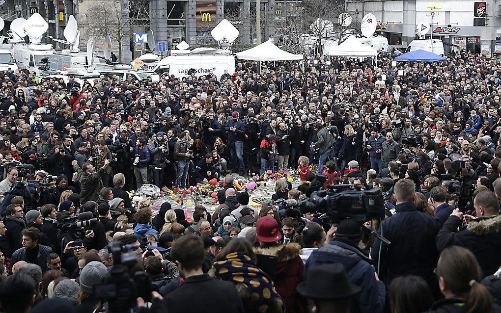 Mensen zijn stil rond een geïmproviseerd gedenkteken op het Beursplein in Brussel. beeld AFP