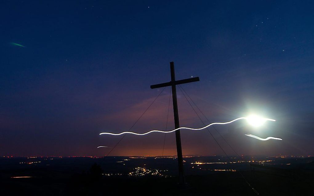 Een man loopt met een hoofdlamp langs een kruis op een berg bij Wenen. Beeld EPA