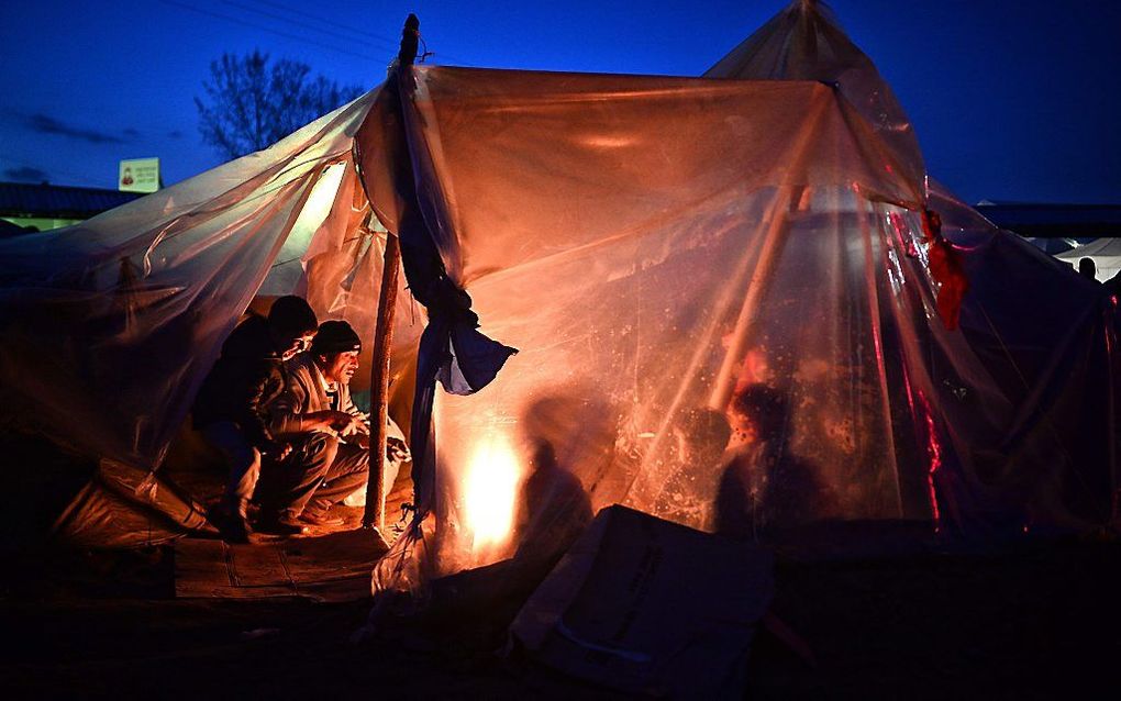 Migranten en vluchtelingen bijeen bij een kampvuur in een tentenkamp bij de Grieks-Macedonische grens. beeld EPA