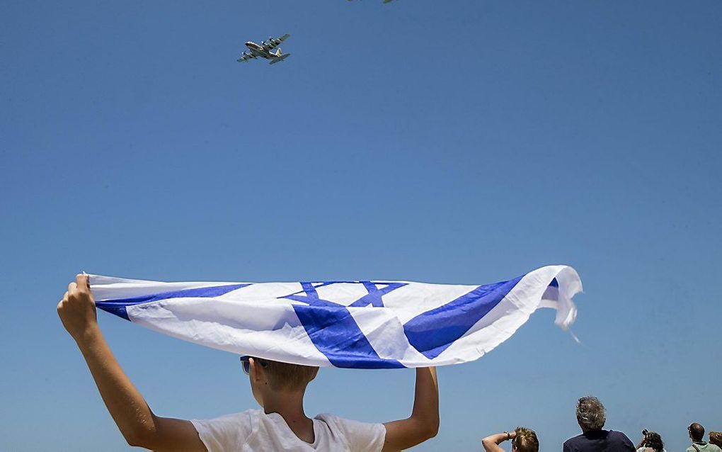 Een jongen in Tel Aviv zwaait met een Israëlische vlag, terwijl Hercules-transportvliegtuigen van de luchtmacht overvliegen. beeld AFP