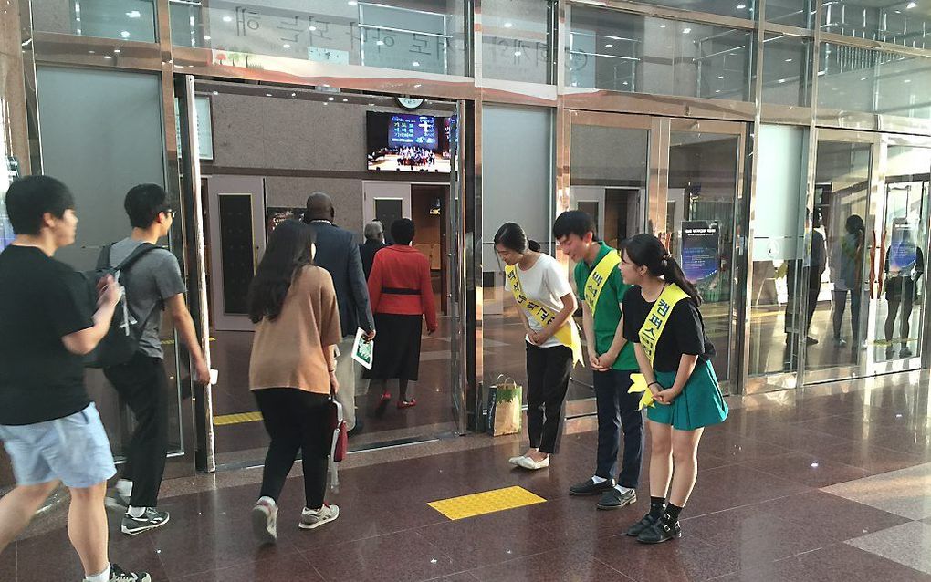 Drie Zuid-Koreaanse jongeren verwelkomen gasten met een buiging bij een dienst in de universiteitskerk in Cheonan. beeld RD