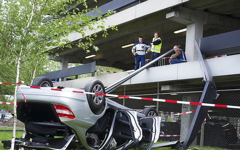 Een auto belandde na de val van de eerste verdieping van het parkeerdek van de luchthaven Schiphol ondersteboven in het gras. Hierbij is een van de drie inzittende om het leven gekomen. Foto ANP