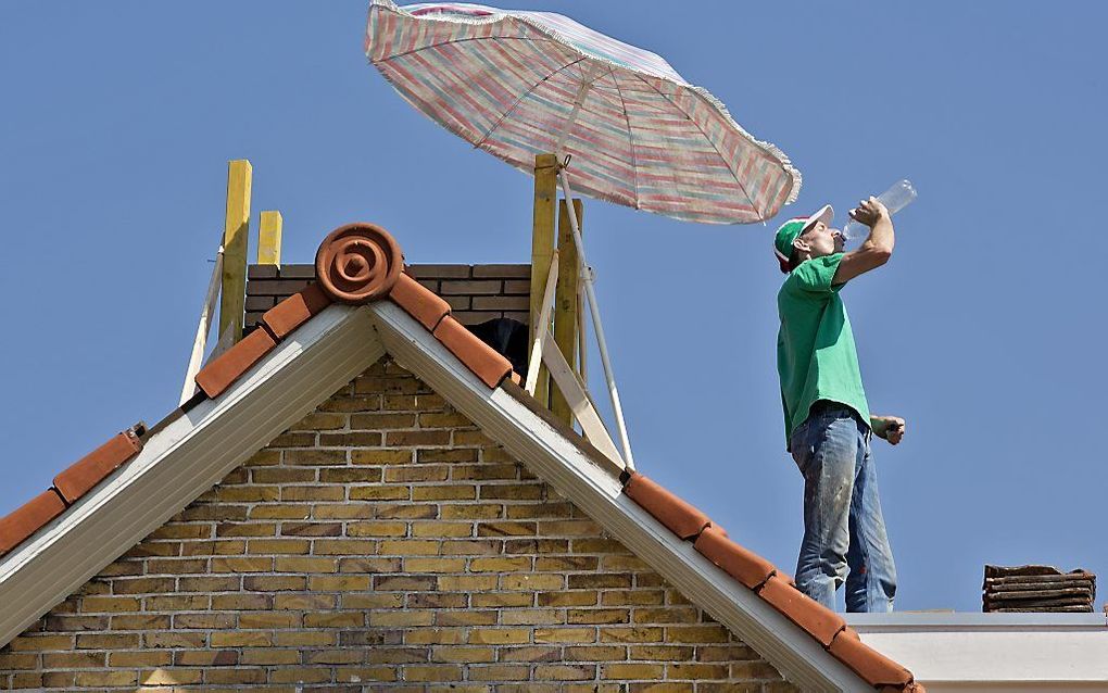 Een metselaar probeert tijdens zijn werkzaamheden op een dak met behulp van een parasol het hoofd koel te houden. Foto ANP