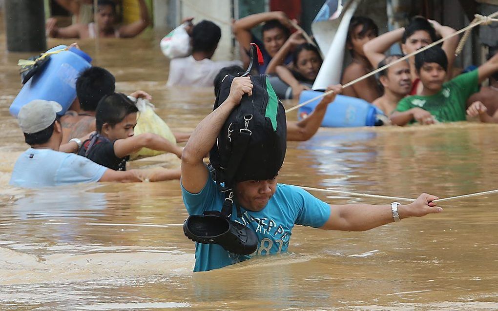 Filipino’s in Marikina proberen met behulp van touwen hun weg te vinden door het water. Foto EPA