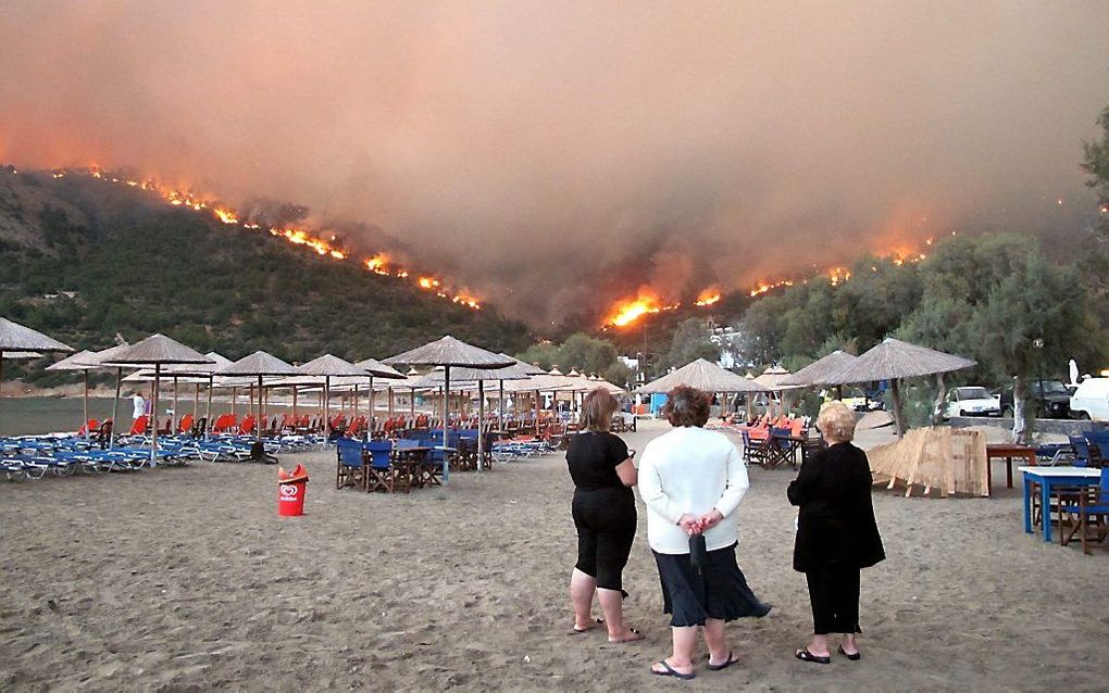 Inwoners van het dorpje Lithi op het eiland Chios bekijken vanaf het strand de bosbrand. Foto EPA