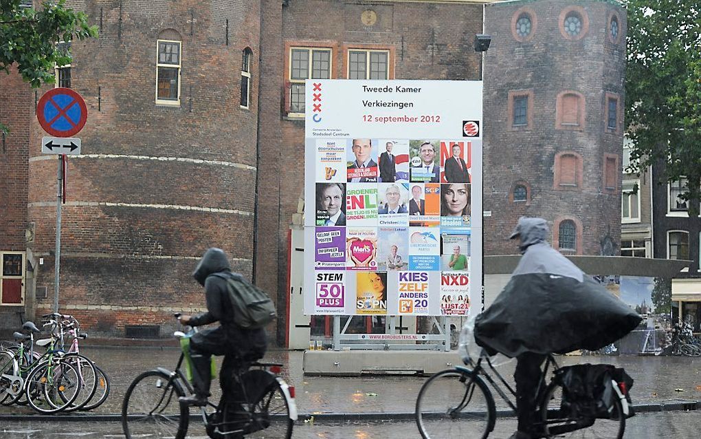 Amsterdammers trotseren de regen, terwijl ze een verkiezingsbord passeren. Foto ANP