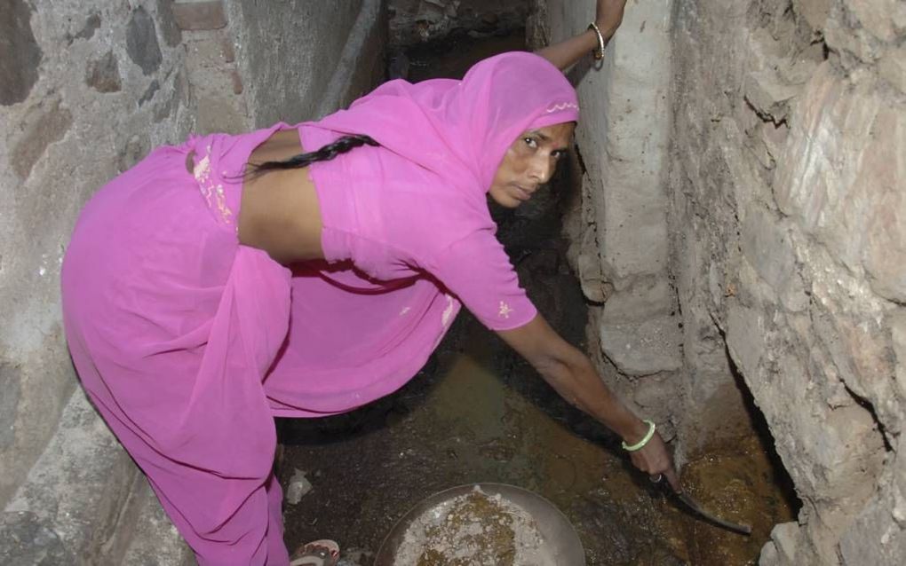 NEW DELHI – Een dalit is bezig met het leeghalen van een privétoilet. Dat doet ze via een luikje aan de buitenkant van een woonhuis. Foto Solutionsforwater.com