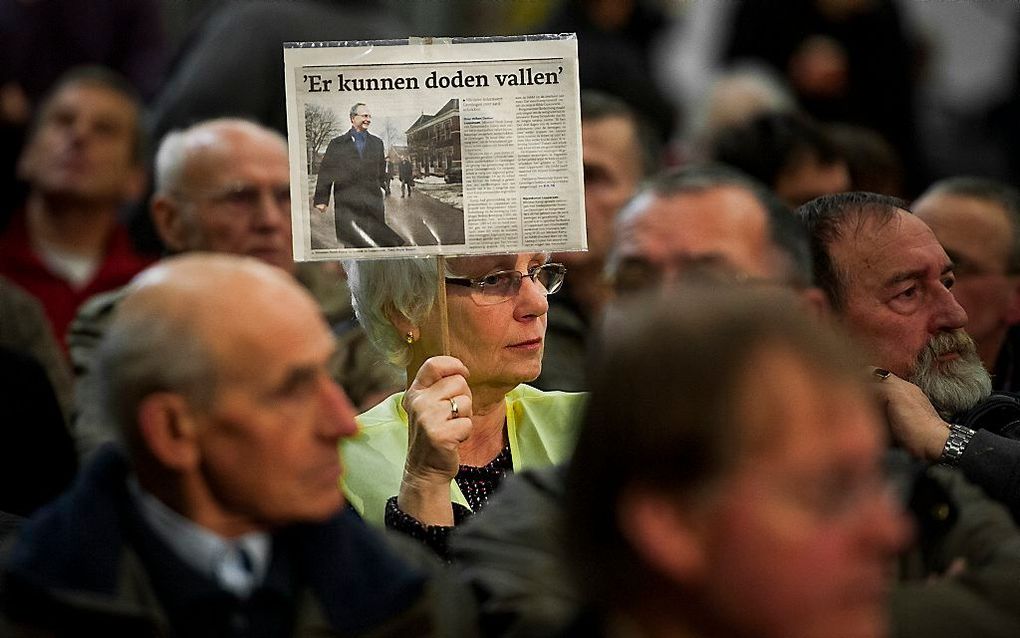 Een bezorgde inwoner houdt een krantenartikel omhoog tijdens een informatiebijeenkomst over de toenemende risico's van aardgaswinning in Noord-Groningen.  Foto ANP