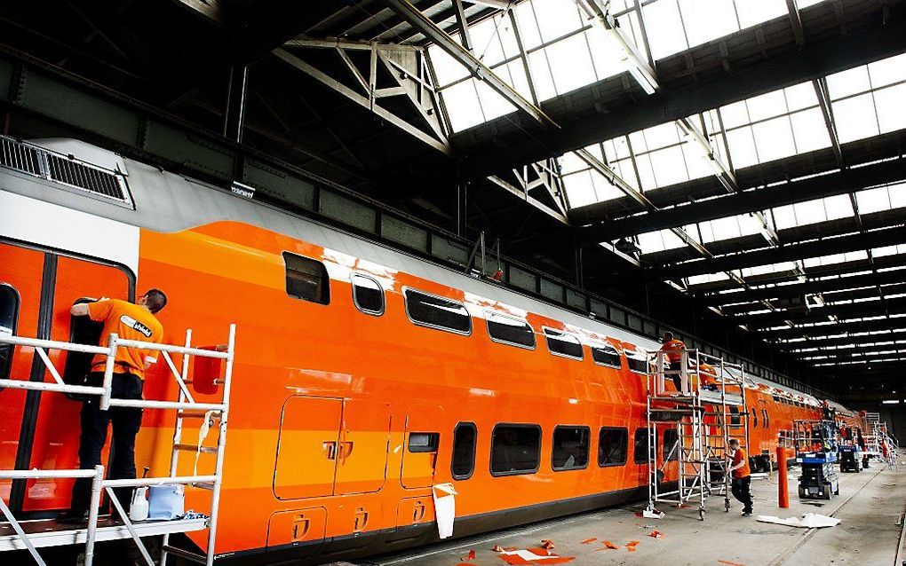 Een trein wordt door medewerkers van de NS voorzien van een oranje folie. Foto ANP