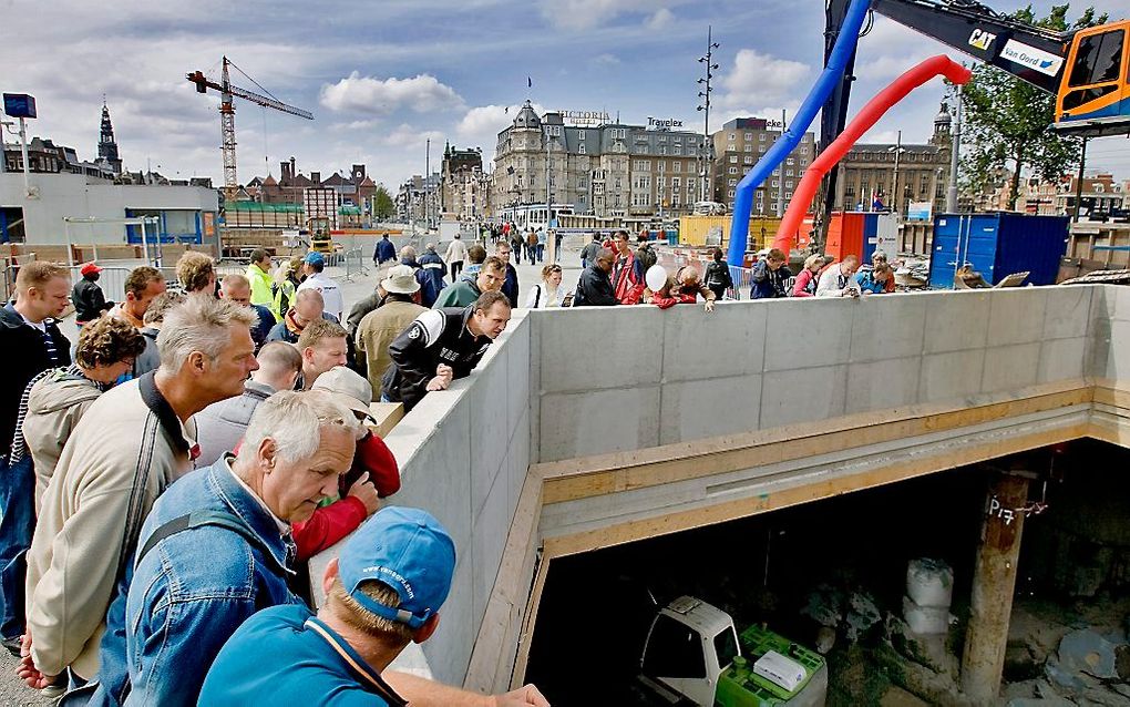 Bezoekers bekijken de bouwplaats voor de Noord/Zuidlijn op het Damrak voor het Centraal Station in Amsterdam. Foto ANP