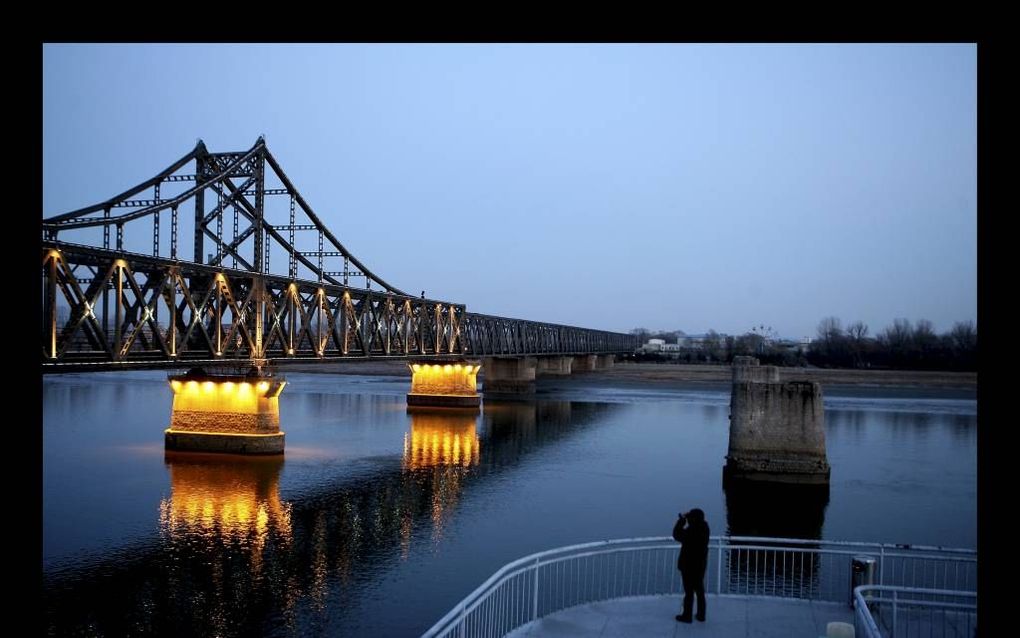 De brug bij de Chinese grensstad Dandong verbindt China met Noord-Korea. Halverwege houdt de verlichting op en begint het deel dat de Noord-Koreanen onderhouden. Toeristen turen er met kijkers naar de overkant. Beeld Henk Visscher