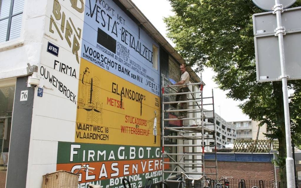 VLAARDINGEN. Kunstenaar Peter de Jong heeft de muurreclames op de hoek van de Hoogstraat en de Afrol hersteld in Vlaardingen. beeld W. den Breems