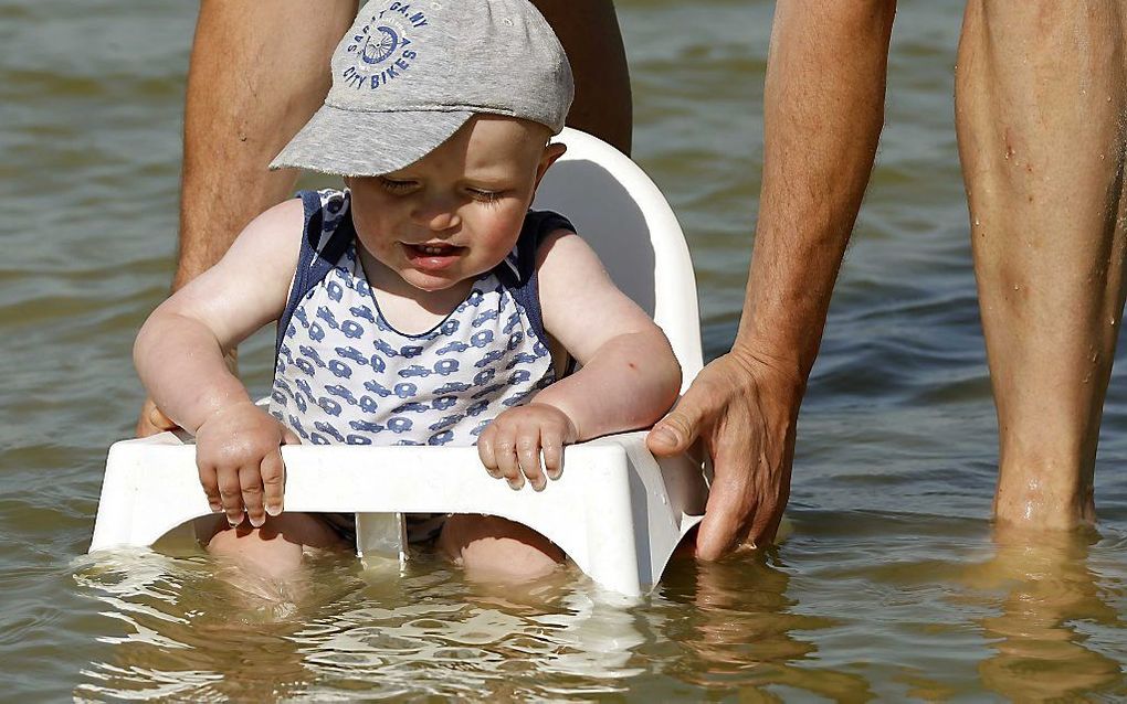 MAKKUM - Een kind wordt ter verkoeling met een kinderstoeltje in het IJsselmeer gezet. De temperatuur is opgelopen tot tropische waarden. beeld ANP