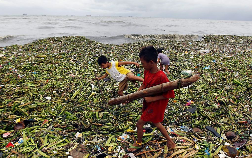 Kinderen spelen tussen aangespoeld materiaal op het strand van een kustdorp bij Manila. Foto EPA