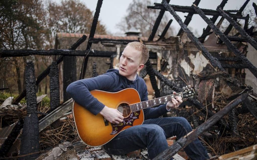 CHE-student Michel Bakker speelt gitaar op de verkoolde ashopen van een woonboerderij in Voorthuizen. Bakker huurde de bovenwoning. Een uitslaande brand legde de boerderij volledig in de as. beeld Dave de Haan