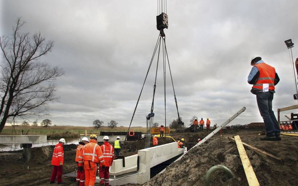 In oranje hesjes gestoken en gehelmde werkers plaatsen de op maat aangeleverde elementen van het eco-aquaduct bij Rouveen. beeld Eelco Kuiken