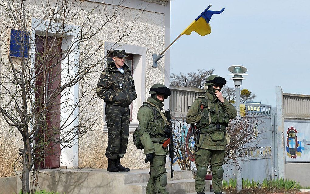 Een Oekraïense officier (l.) staat achter Russische militairen, die een basis in Perevalnaje, in de buurt van Simferopol blokkeren. beeld AFP