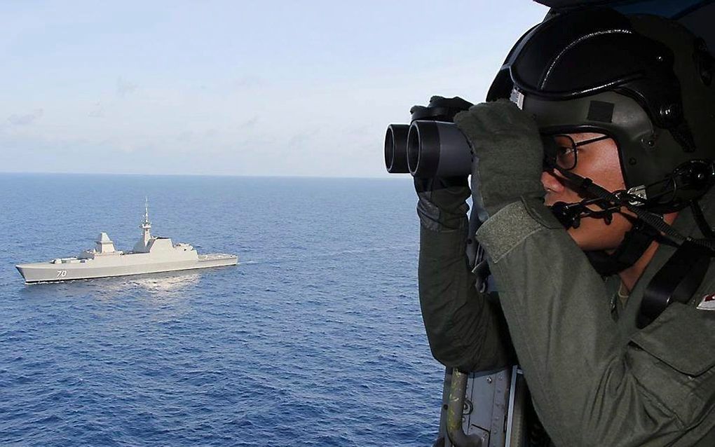 Een militair van de luchtmacht van Singapore speurt vanuit een helicopter naar wrakstukken van de vermiste Boeing 777. Foto EPA