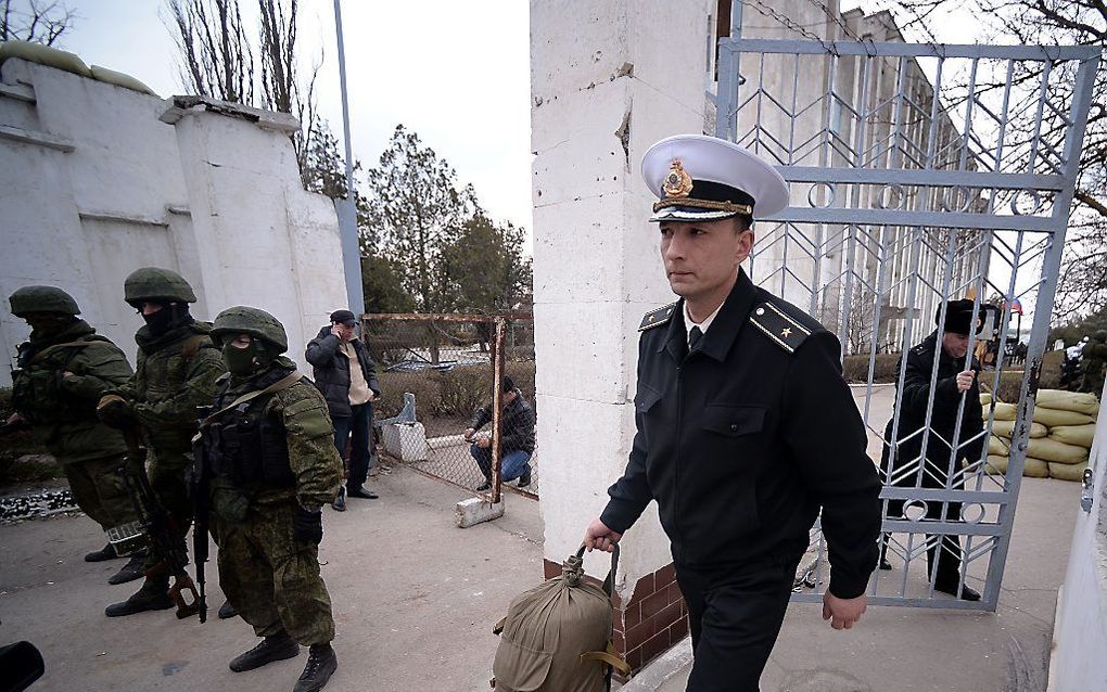 Een Oekraïnse officier verlaat gedwongen zijn basis in Novoozerne, terwijl de Russen toekijken. Foto AFP